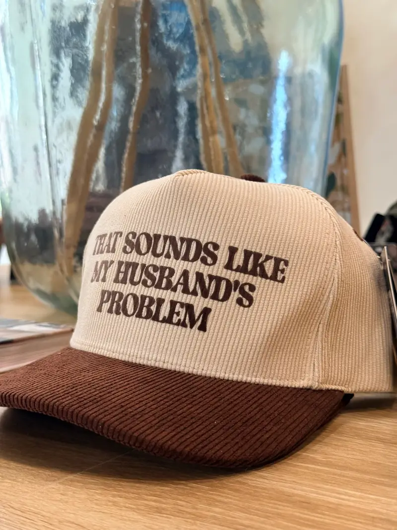 A cream and brown corduroy trucker hat reading “That sounds like my husband’s problem”