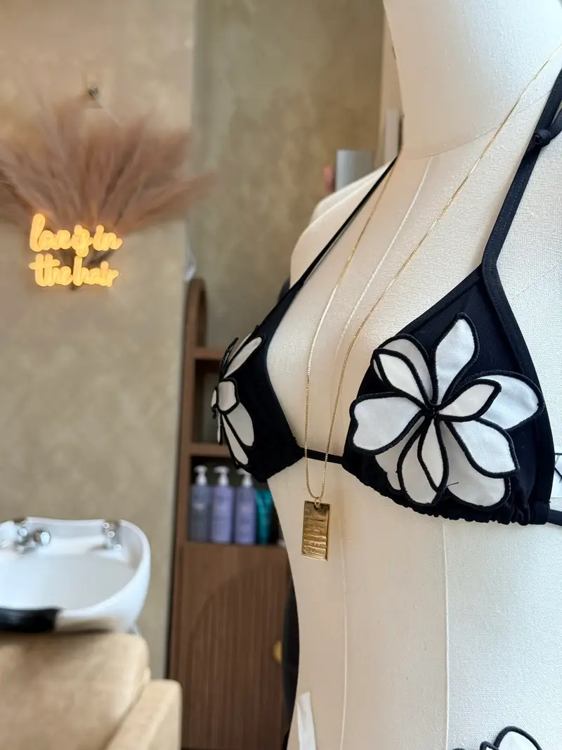 A black cut-out swim top on a dress form beside a gold pendant necklace, under the salon's neon sign
